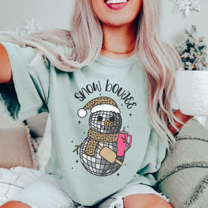 Oversized pale green Comfort Colors tshirt. Disco ball snowman with a leopard print Santa hat and scarf with a buckle bag and pink water cup. Festive Christmas snowman shirt for Holiday parties.