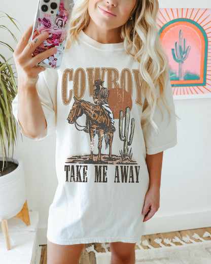 Model is in an oversized ivory crewneck t-shirt featuring a rustic country western graphic in neutral tones. Graphic contains a cowboy at sunset in the desert with the words, cowboy take me away.