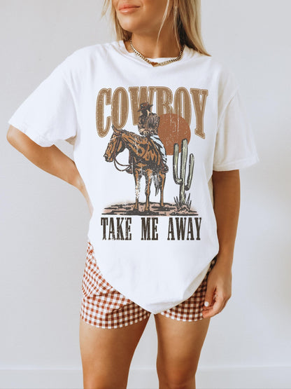 Model is in an oversized white crewneck t-shirt featuring a rustic country western graphic in neutral tones. Graphic contains a cowboy at sunset in the desert with the words, cowboy take me away.