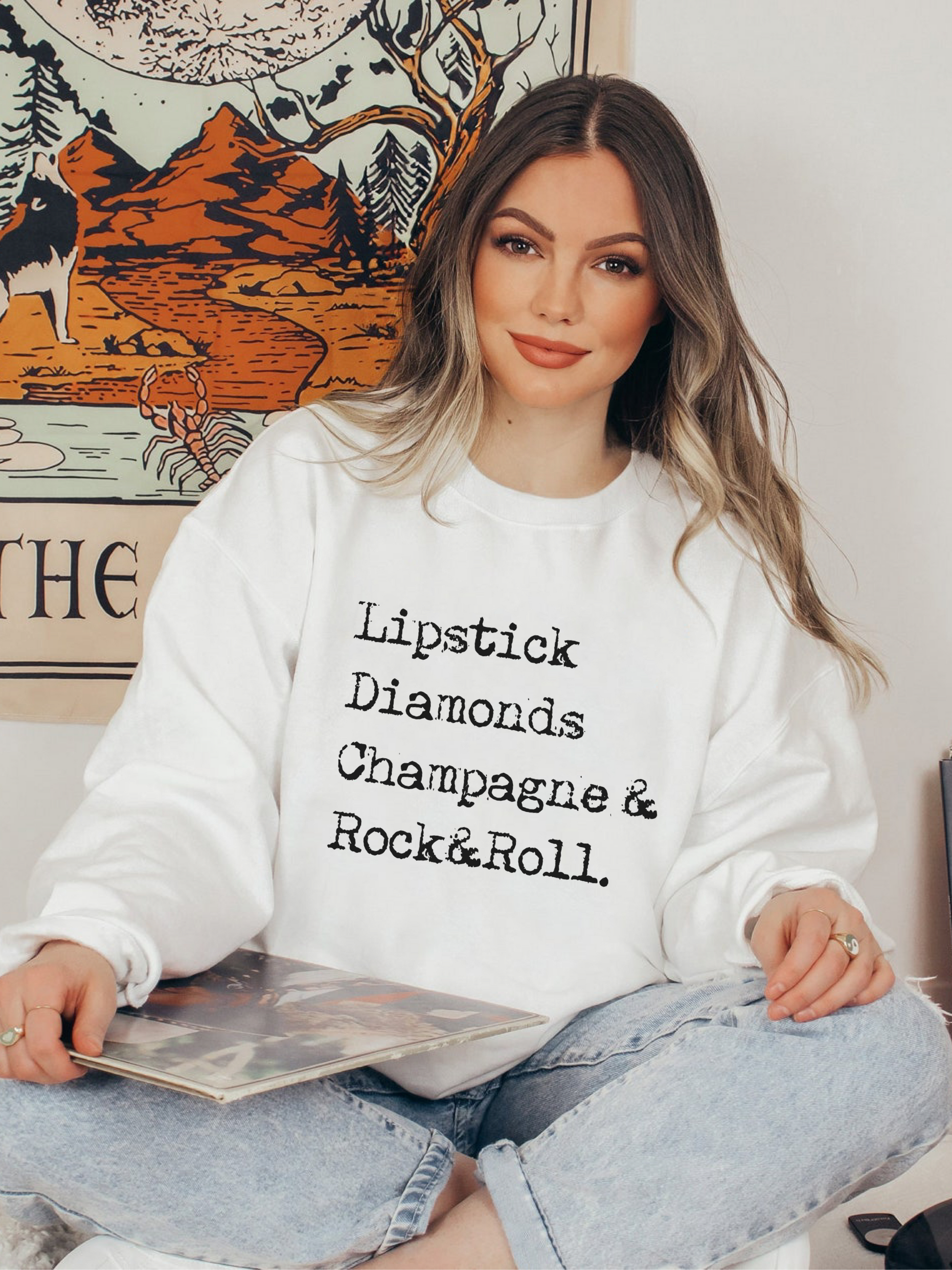 Model wearing white crewneck with distressed rock and roll, champagne, lipstick and diamonds graphic
